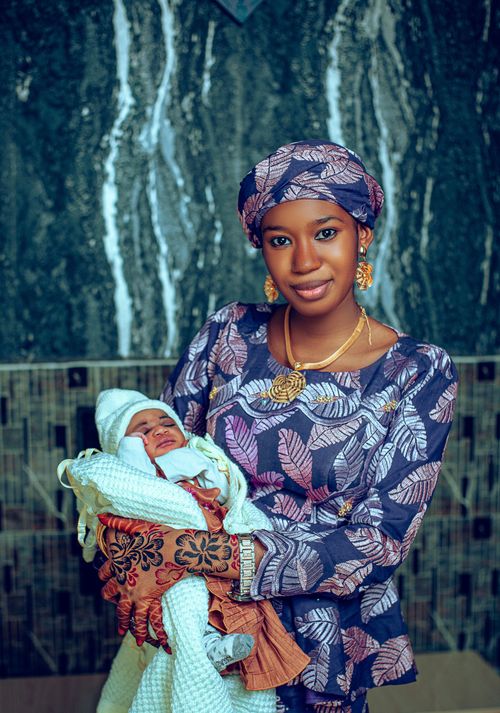 Free A woman in traditional attire lovingly holds a newborn baby indoors. Stock Photo