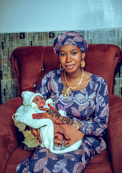 Free A mother holding her newborn in vibrant traditional attire, seated indoors. Stock Photo