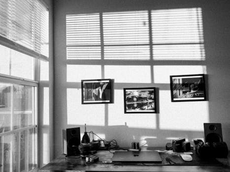Monochrome office setup with shadows, art frames, and camera gear.