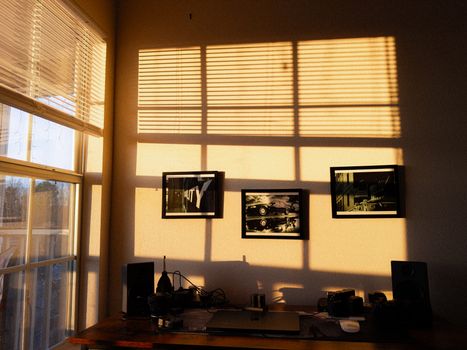 A home office with a wooden desk bathed in warm sunlight, featuring a tidy minimalist setup.