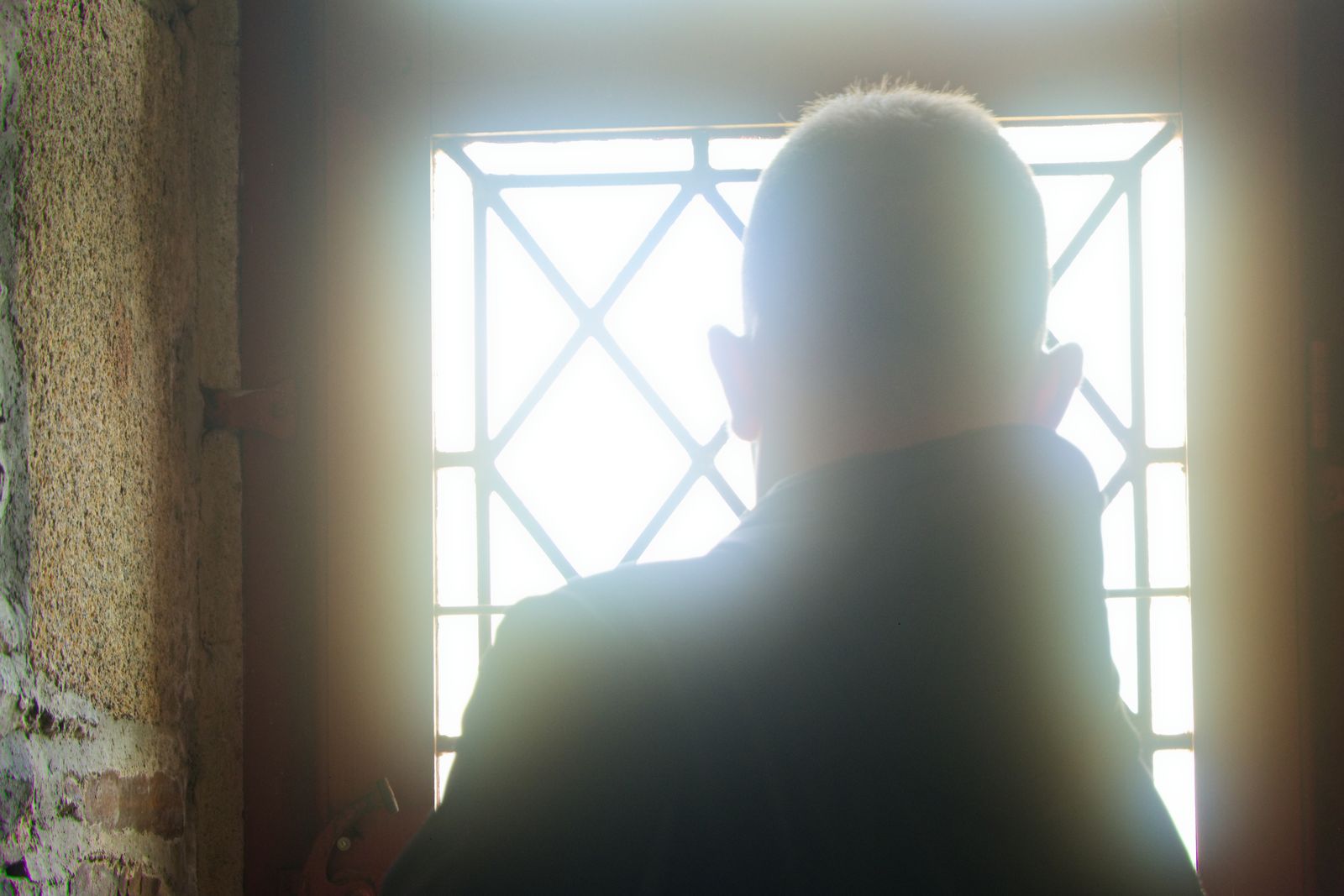 Silhouette à contre-jour d'un homme vu de dos face à une fenêtre à croisillons