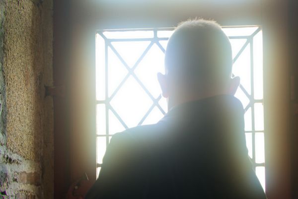 Silhouette à contre-jour d'un homme vu de dos face à une fenêtre à croisillons