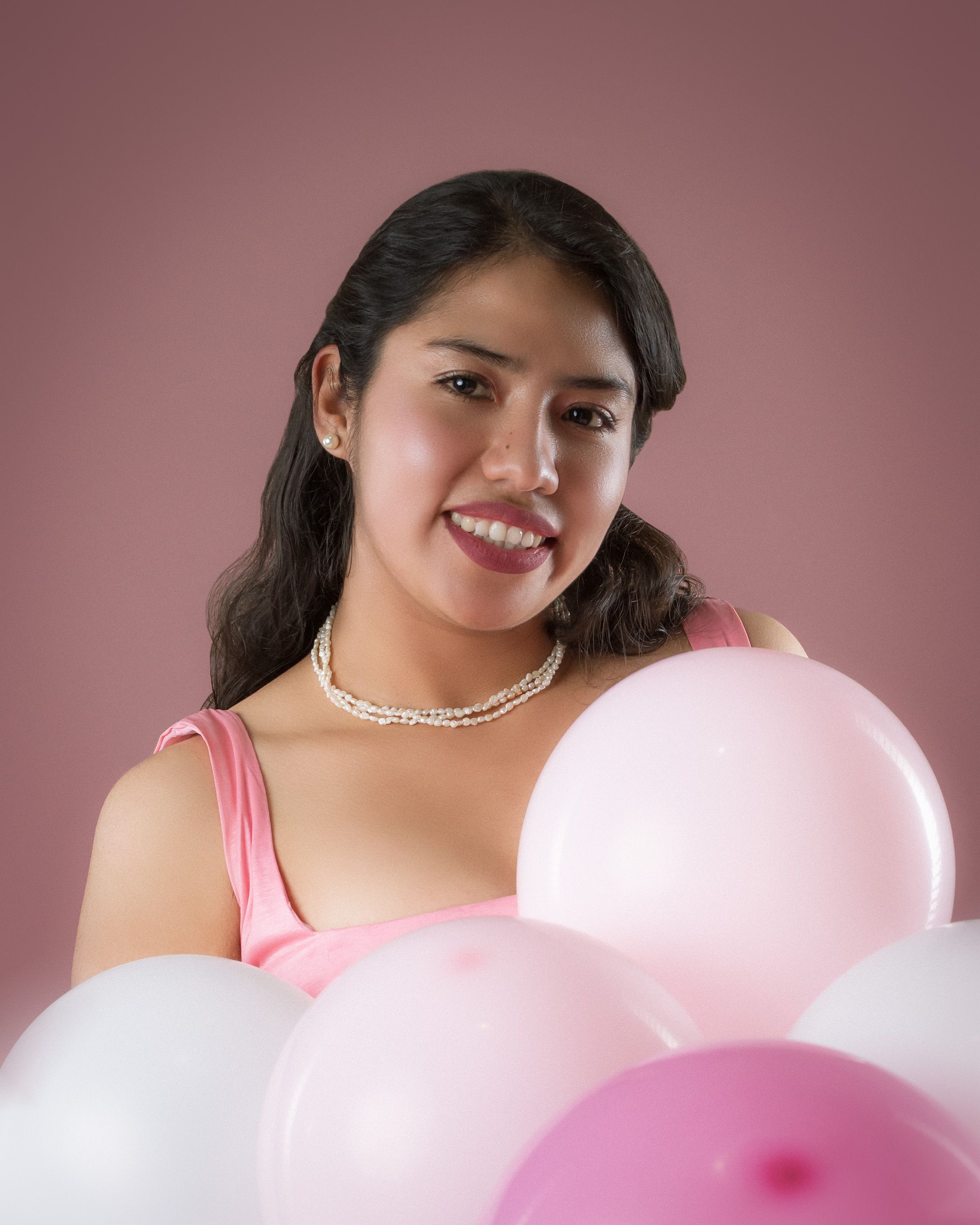 Young woman in pink with balloons, smiling and cheerful.