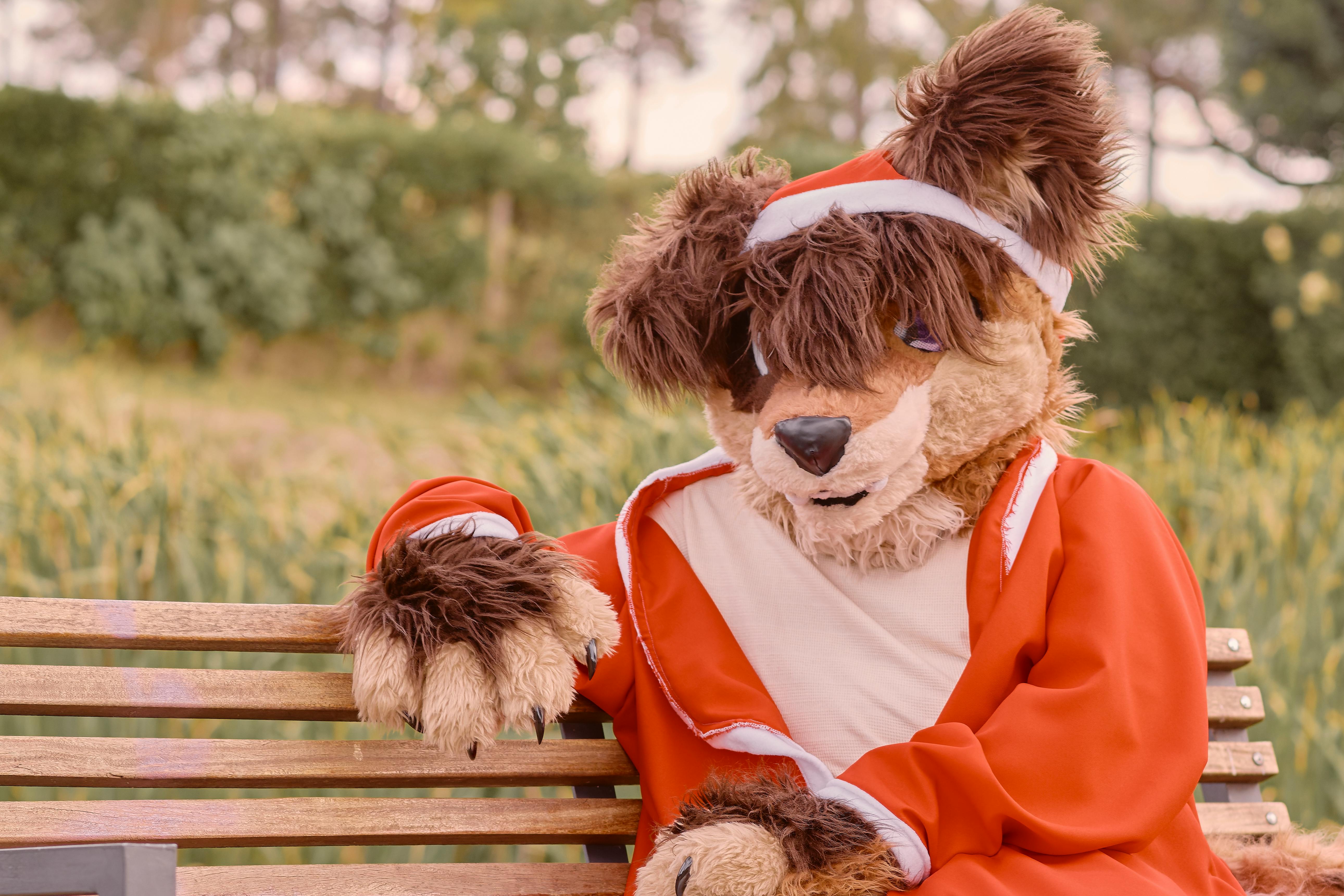A person in a furry costume sits on a park bench, creating a playful outdoor scene.