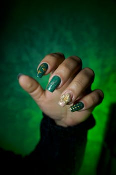 Hand displaying stylish green and gold nail art with a flower accent.