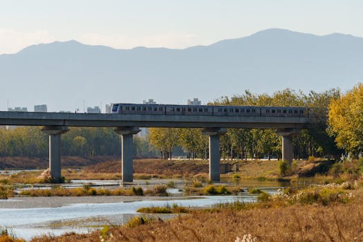 A modern train traverses a bridge with a scenic mountain backdrop near Beijing, China.