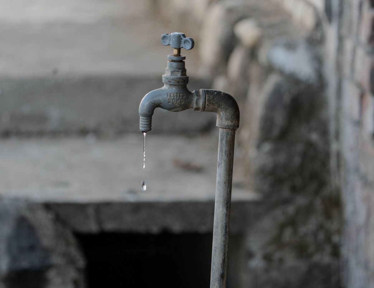 A close-up of a rustic outdoor faucet dripping water against a natural, textured background, symbolizing scarcity.