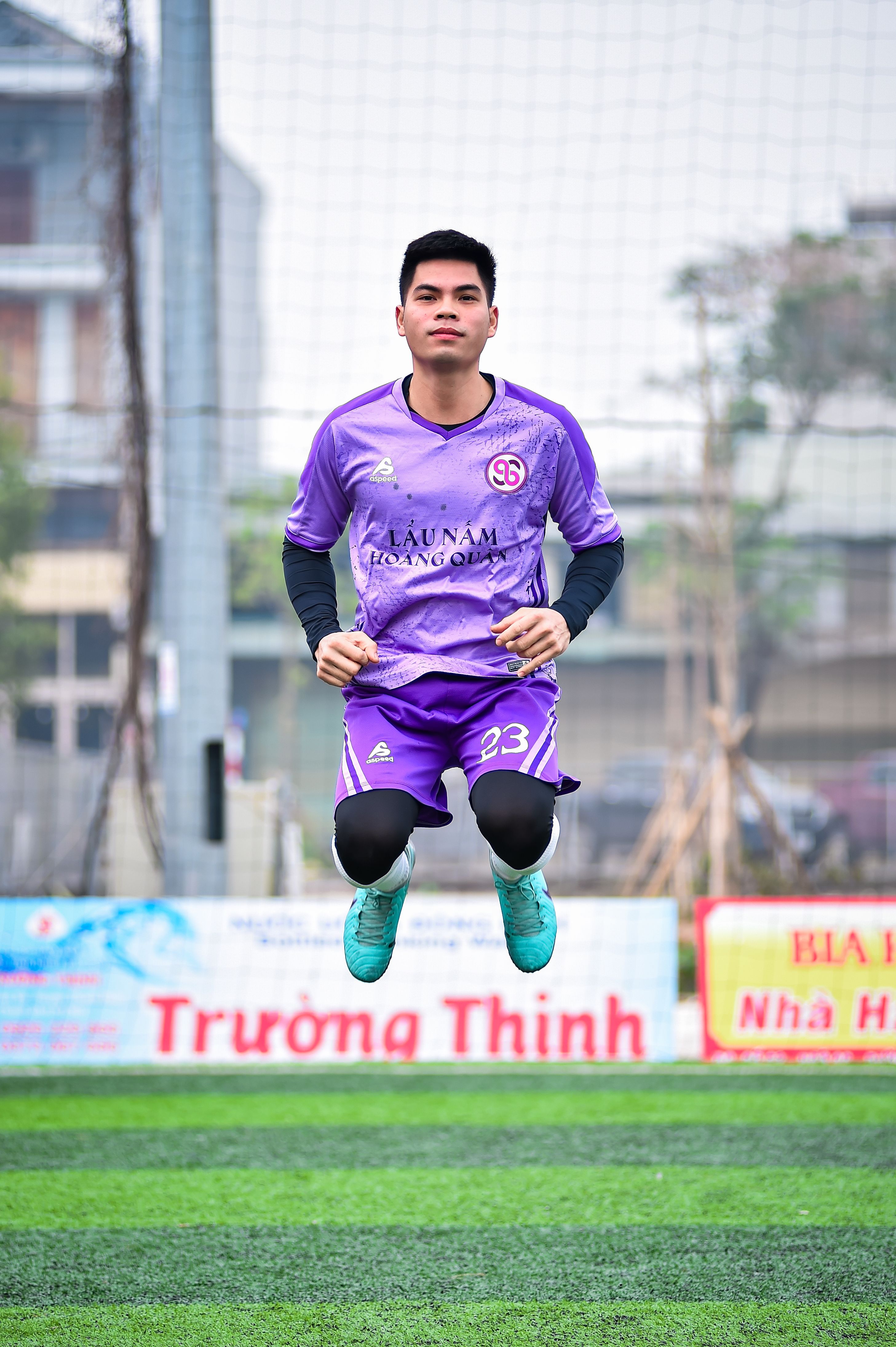 Asian football player in mid-air leap on artificial turf field in Hanoi, Vietnam.