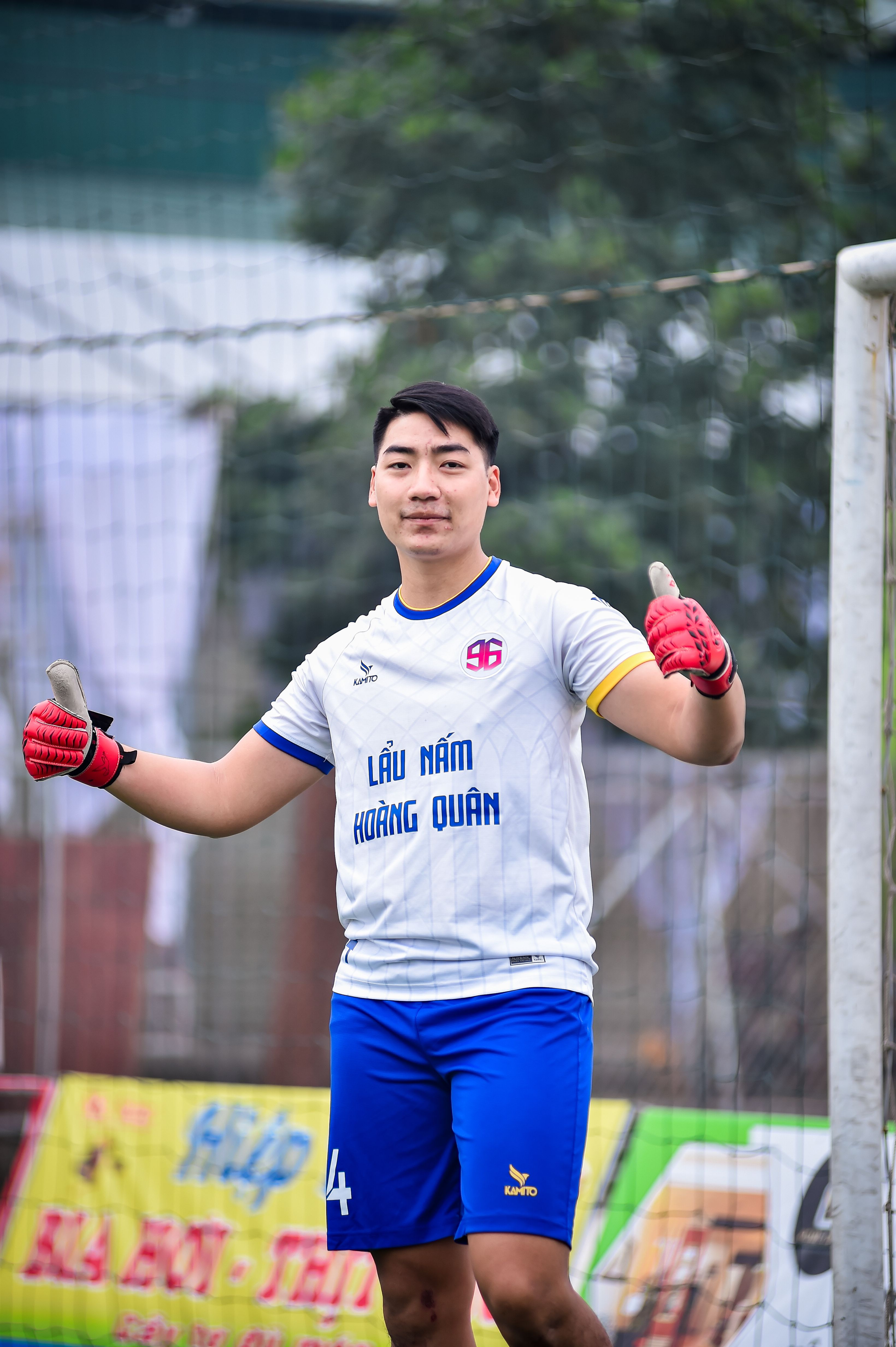 Young adult goalkeeper in sports uniform and gloves giving a thumbs up on a football field.