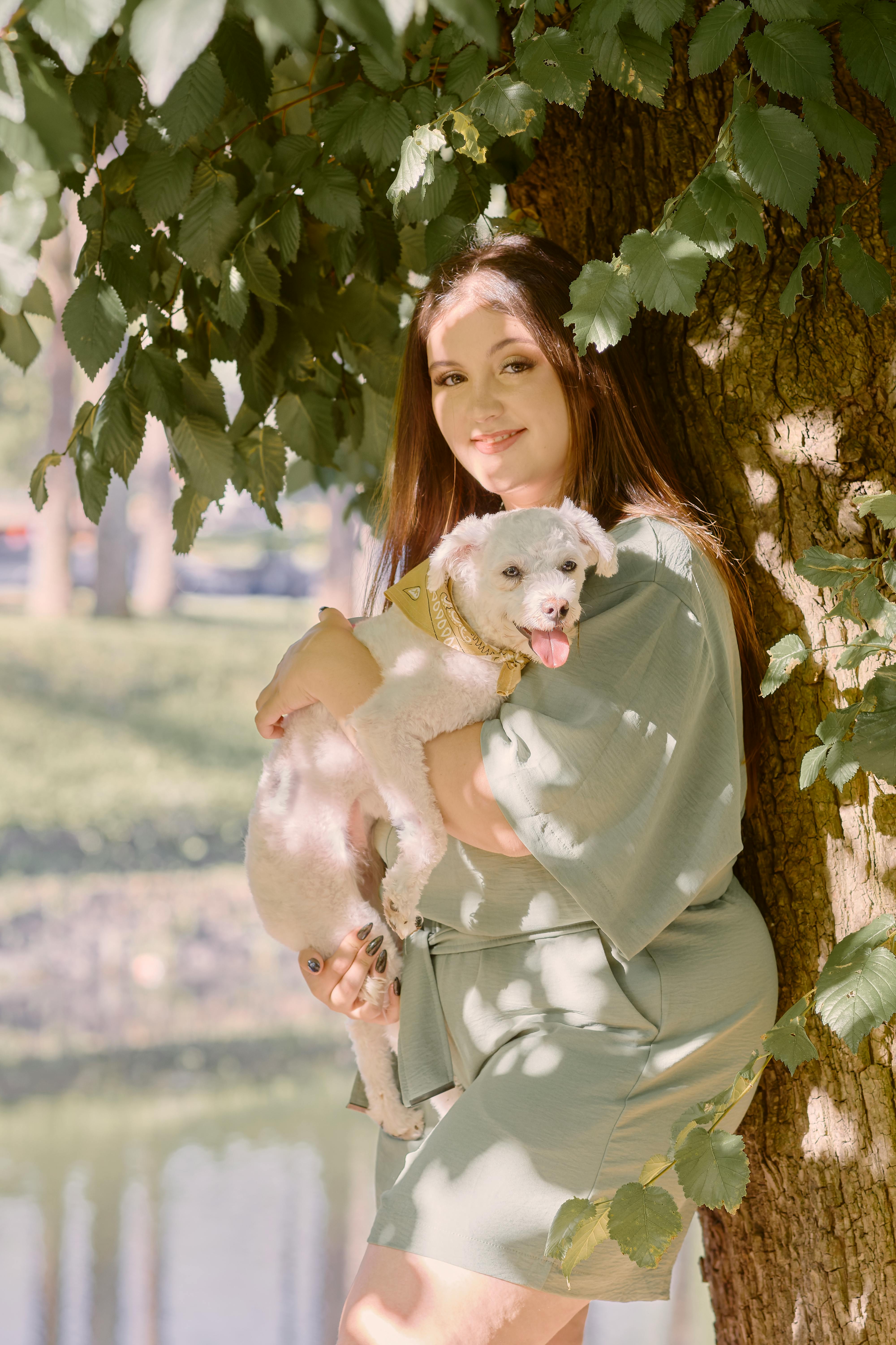 A woman enjoys a sunny day outdoors, hugging her dog under a lush green tree.