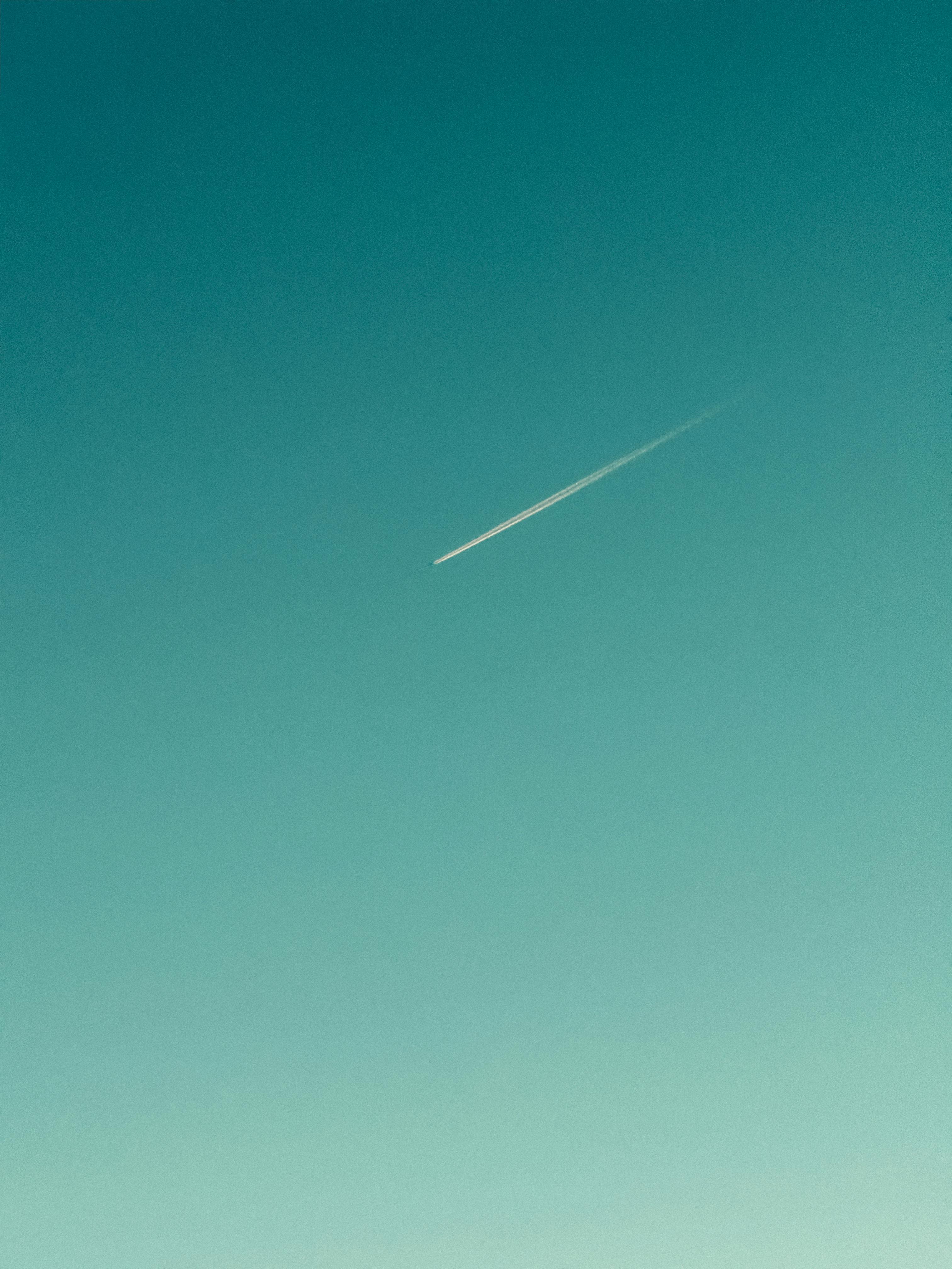 A sleek jet contrail streaks across a clear blue sky, offering a serene minimalist view.
