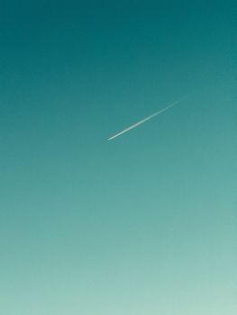 A sleek jet contrail streaks across a clear blue sky, offering a serene minimalist view.
