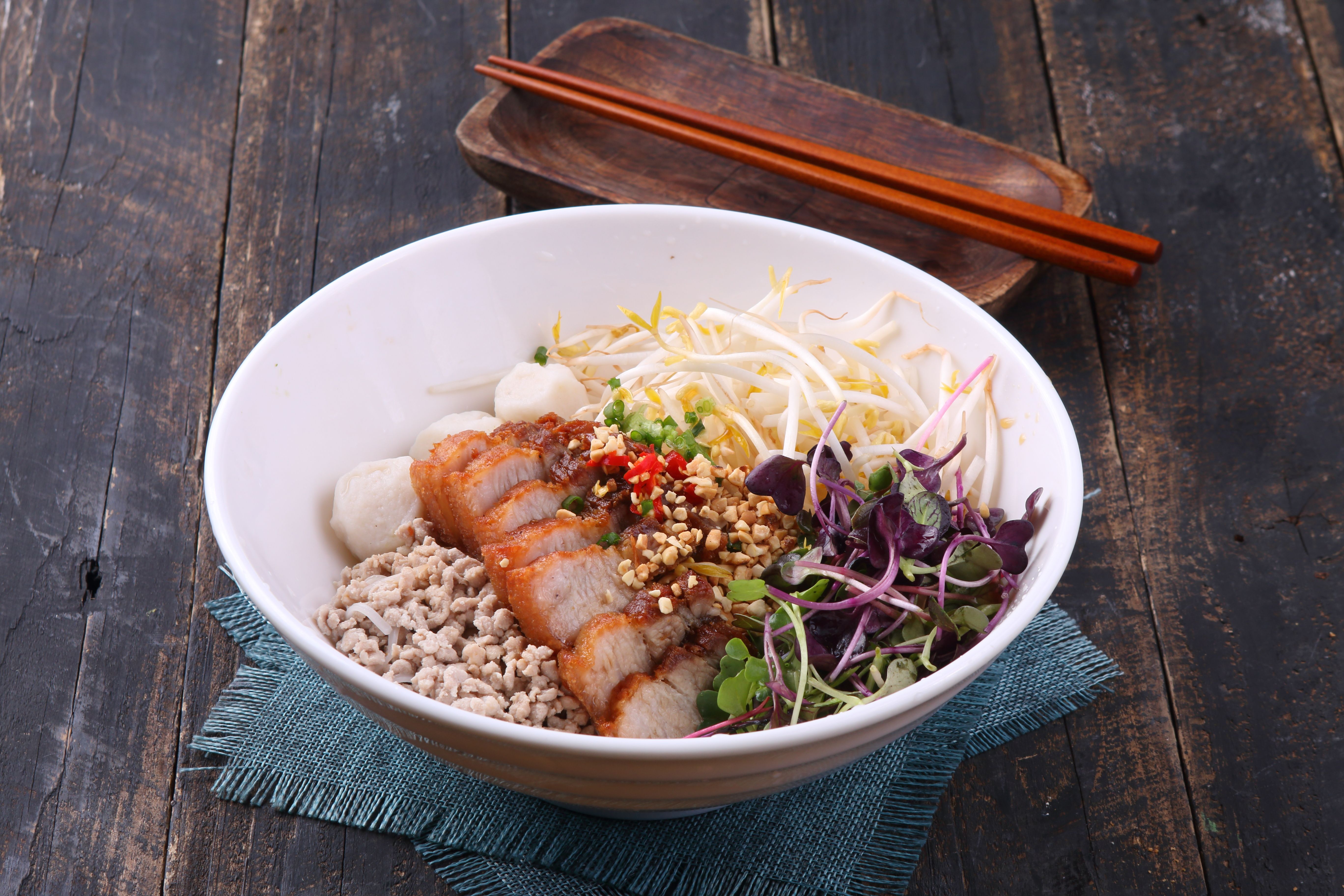 Bowl of wheat noodles coated in glossy red chili oil sauce, topped with crispy ground pork and chopped green scallions