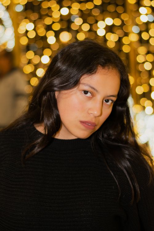 Free Poised young woman with dark hair in front of glowing bokeh lights, creating a warm and festive vibe. Stock Photo