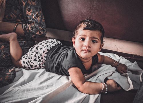 Free A cute baby in patterned shorts and dark shirt crawling indoors with a playful expression. Stock Photo