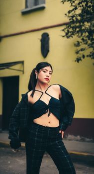 Confident woman posing in trendy outfit against a city wall outdoors.