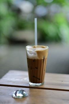 Refreshing iced coffee with frothy foam on wooden table, perfect for summer.