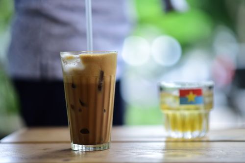 Free Close-up of a refreshing iced coffee with a straw on a wooden table outdoors. Stock Photo