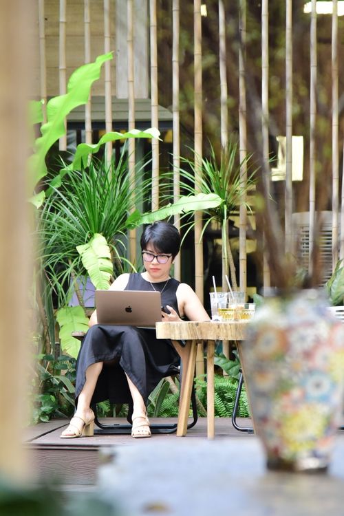 Free A woman sits in an indoor garden cafe, working on a laptop amidst lush greenery and modern decor. Stock Photo