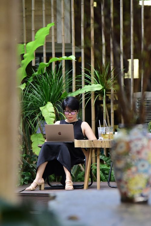 Free A woman sits in a lush garden, focused on her laptop, surrounded by greenery and decorative elements. Stock Photo