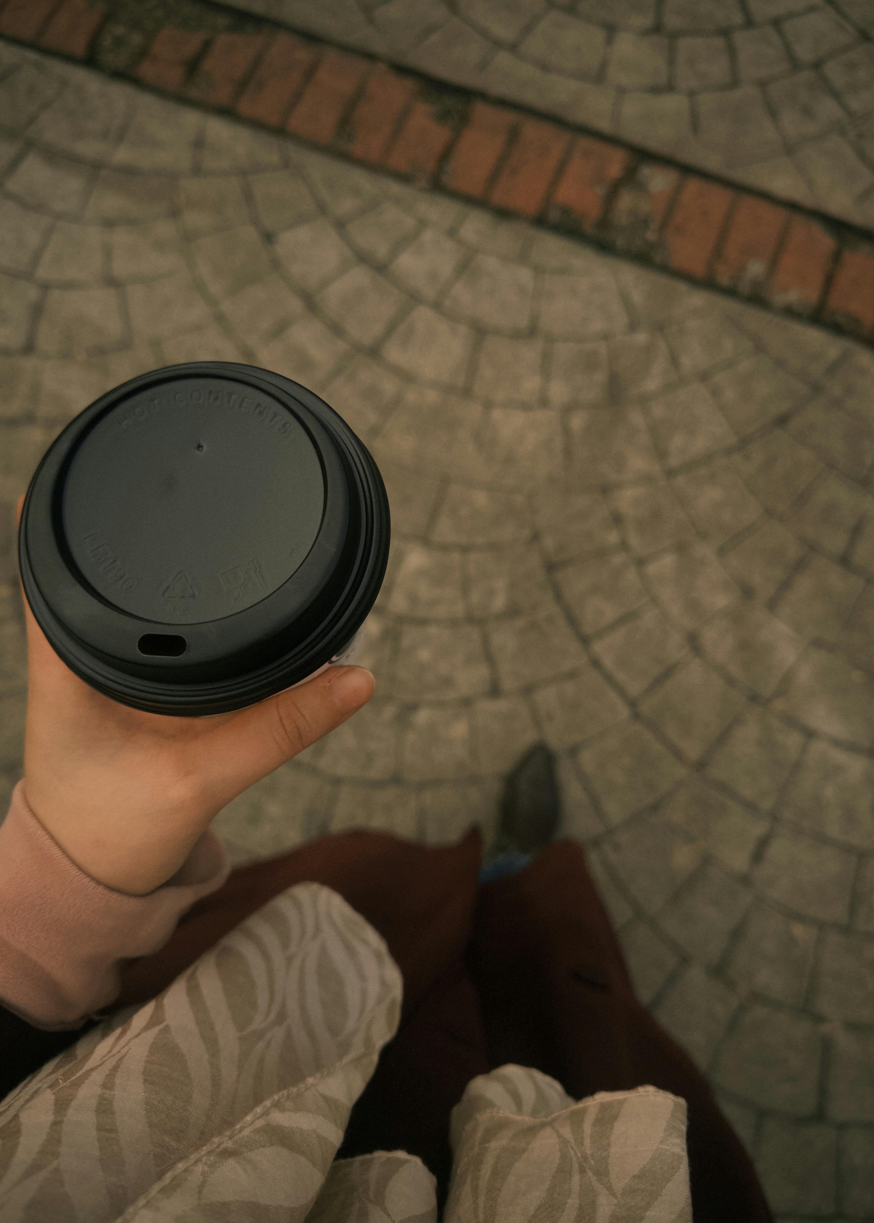 Gratuit Vedere de sus a unei persoane care ține o ceașcă de cafea la pachet pe o alee pietruită cu model. Fotografie de stoc