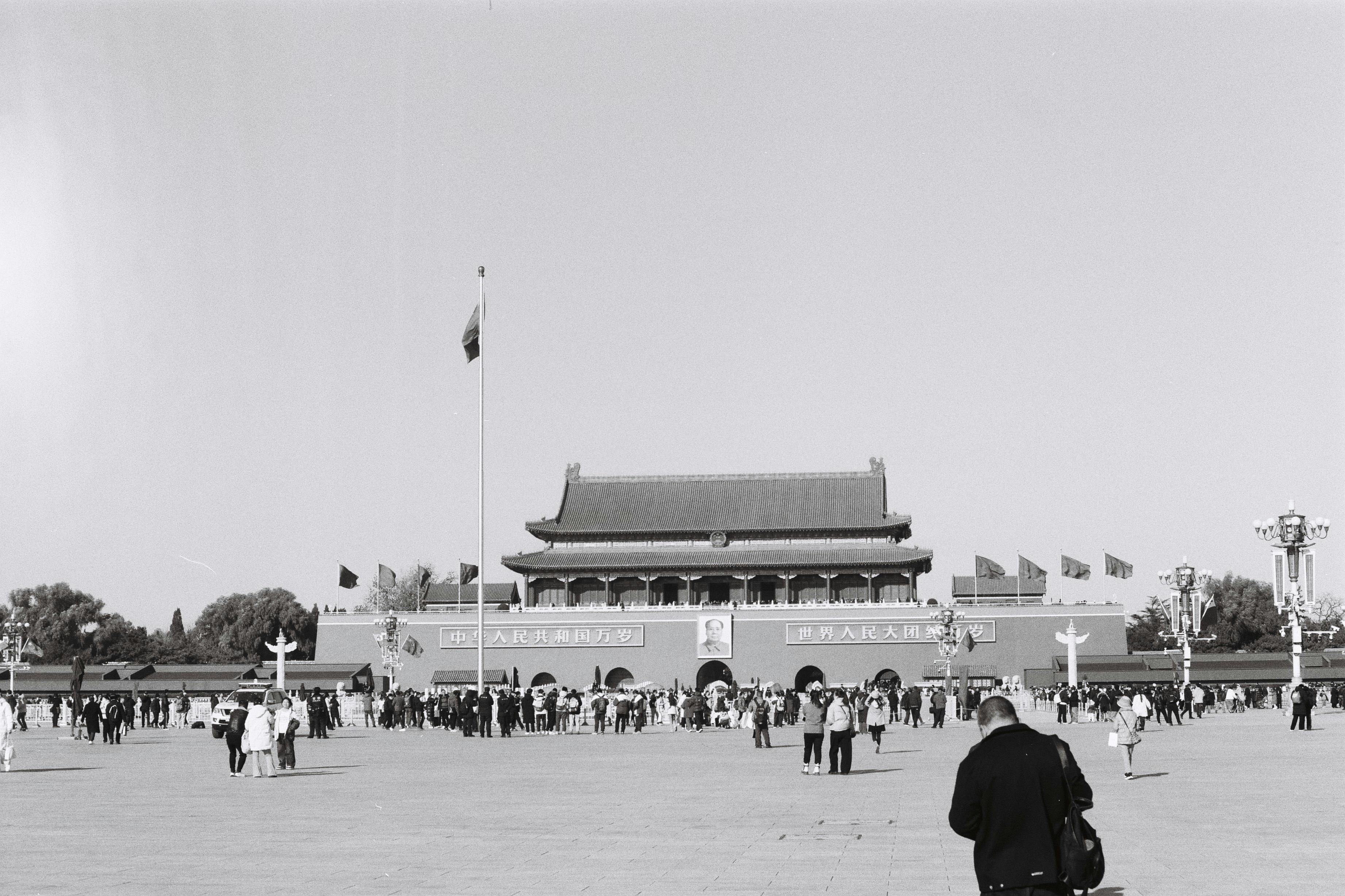 Crowds at Tiananmen Square with the iconic gate and flagpole in a monochrome setting.