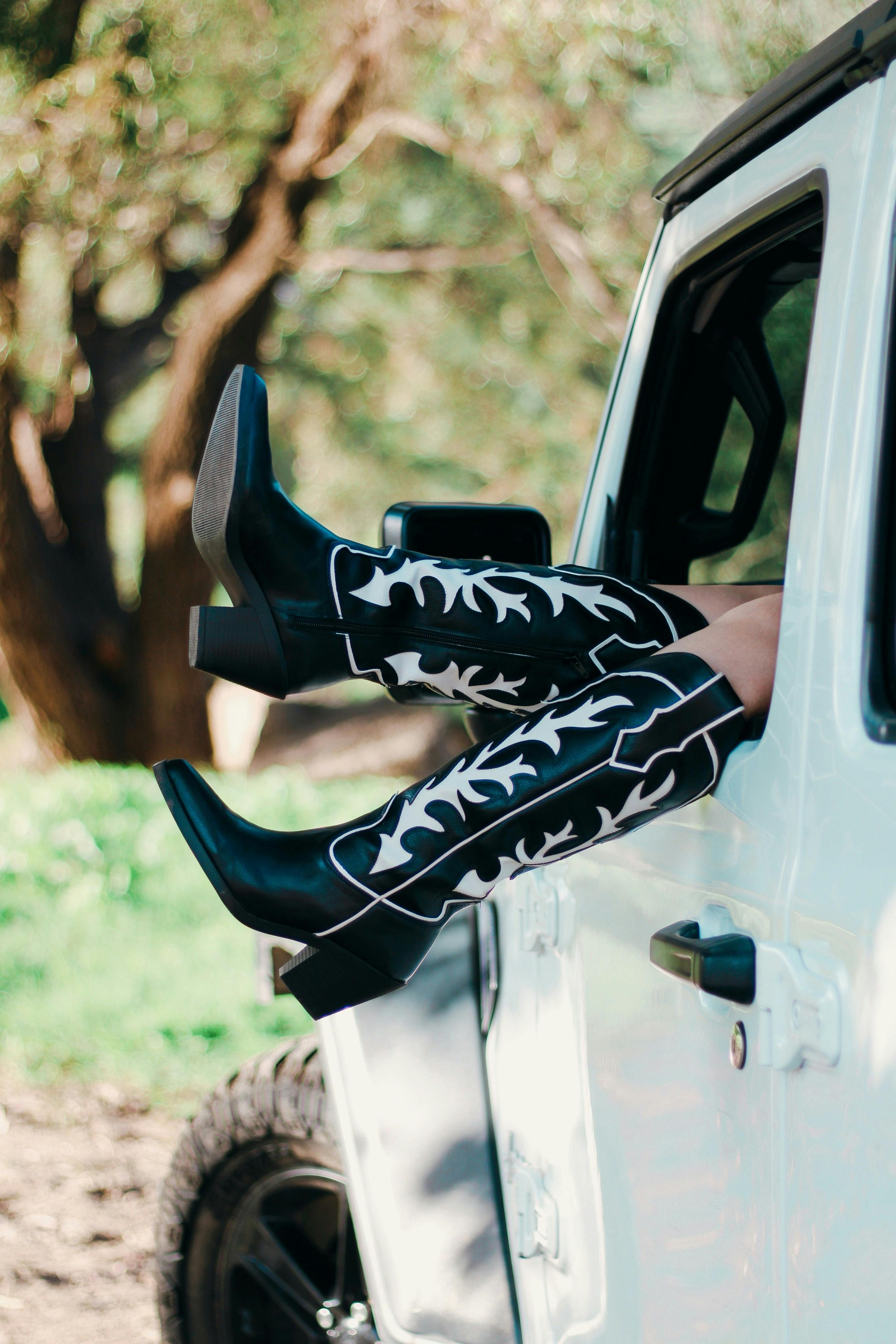 Stylish cowboy boots sticking out of a white car, outdoors on a sunny day.