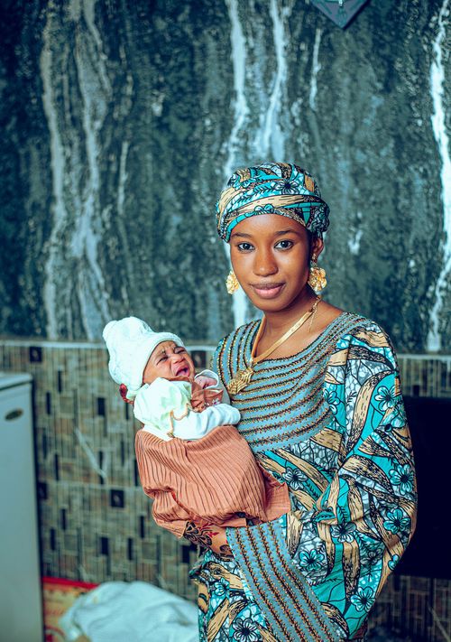 Free African woman in traditional attire holding a newborn baby indoors. Stock Photo