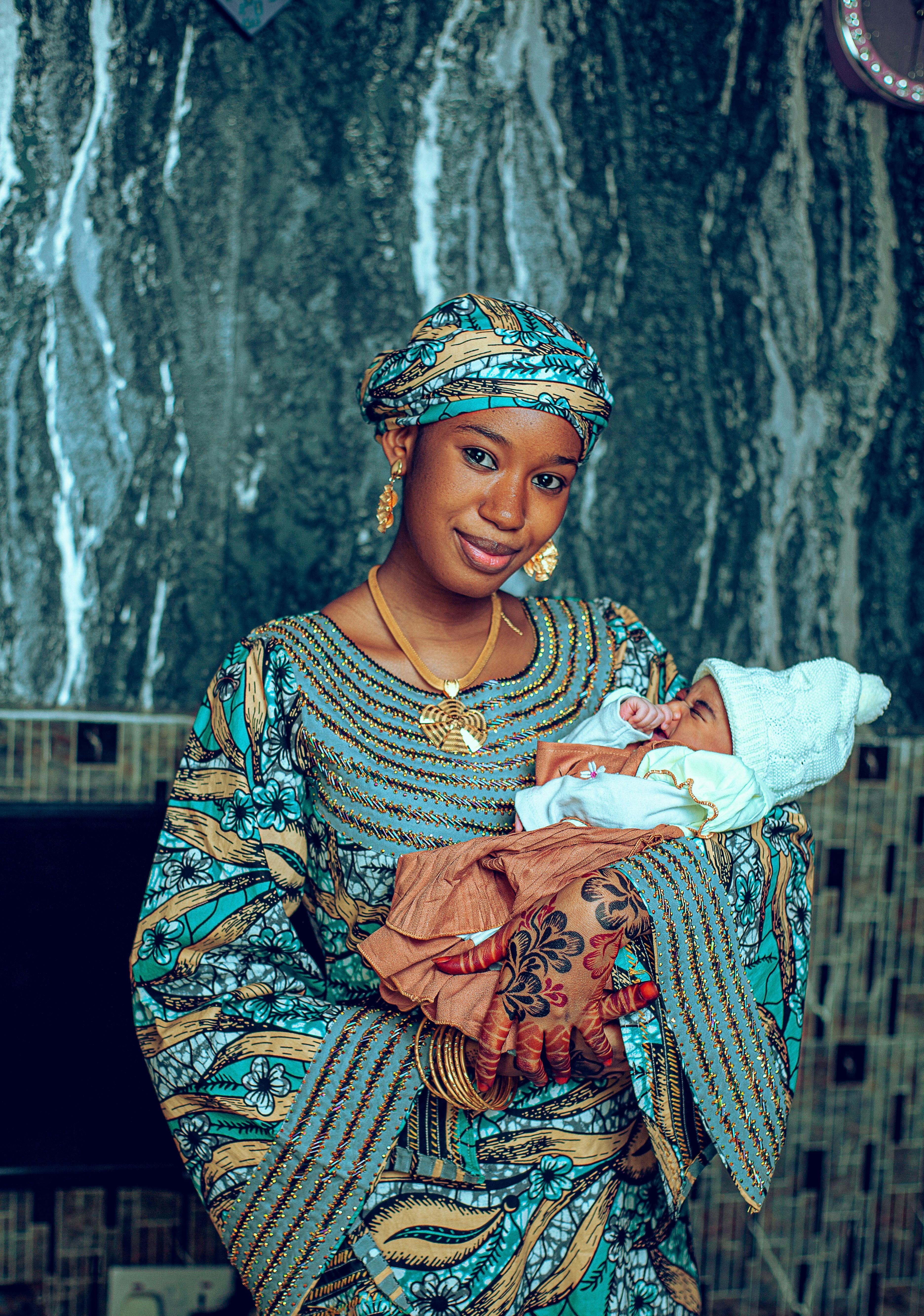 Smiling mother in colorful attire cradling a newborn indoors. Warm and joyful moment captured.