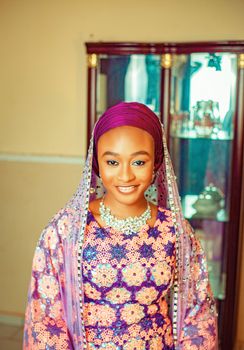 Smiling woman in vibrant traditional dress with jewelry indoors.