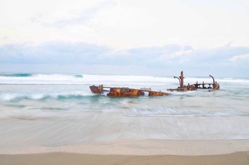 Free Scenic view of a rusted shipwreck on a serene beach under pastel skies. Stock Photo