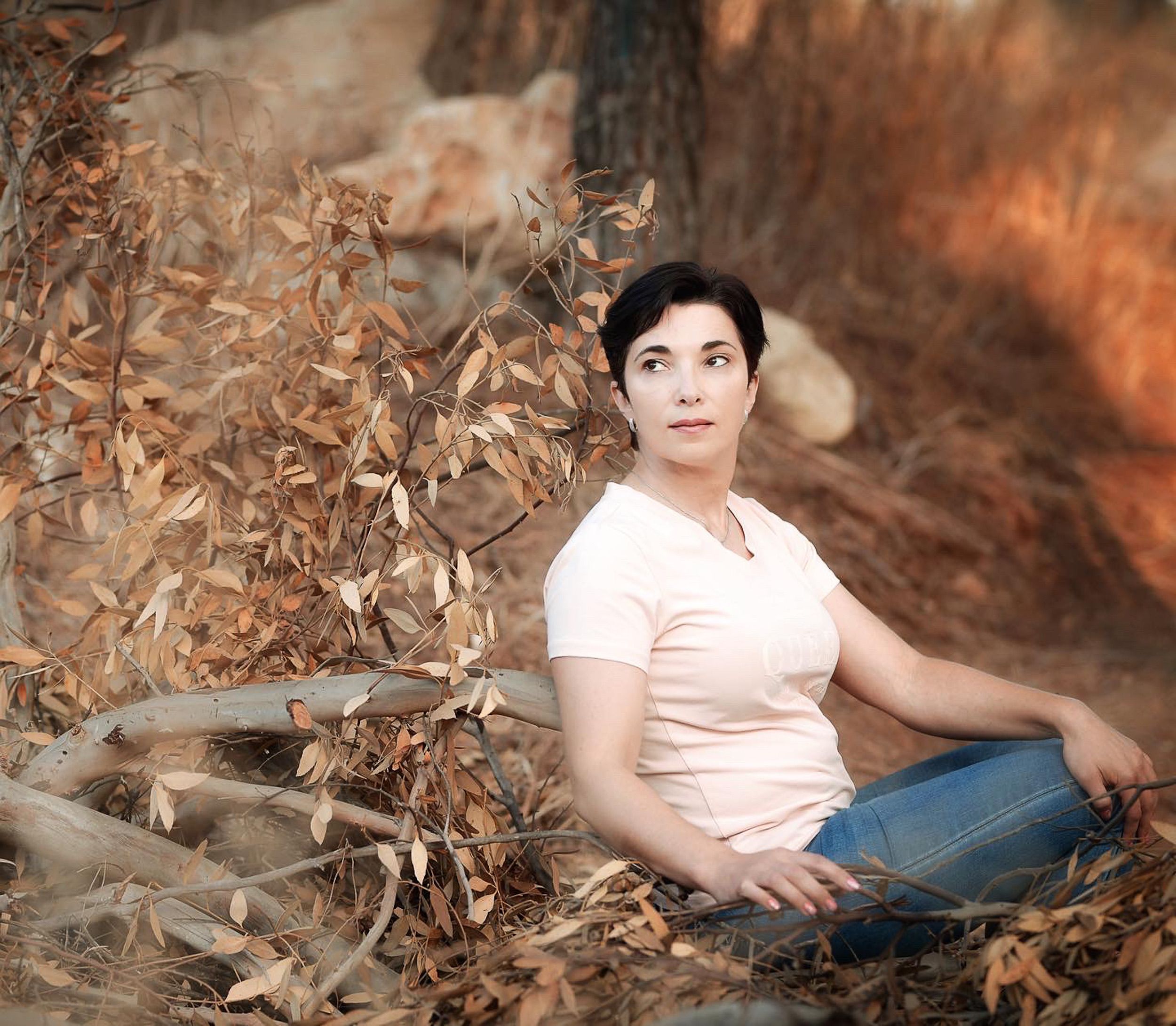 Woman seated in an autumn forest surrounded by dry leaves and trees, serene and peaceful.