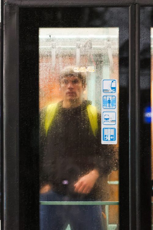 Free Man with a yellow backpack stands behind wet glass on public transport. Stock Photo