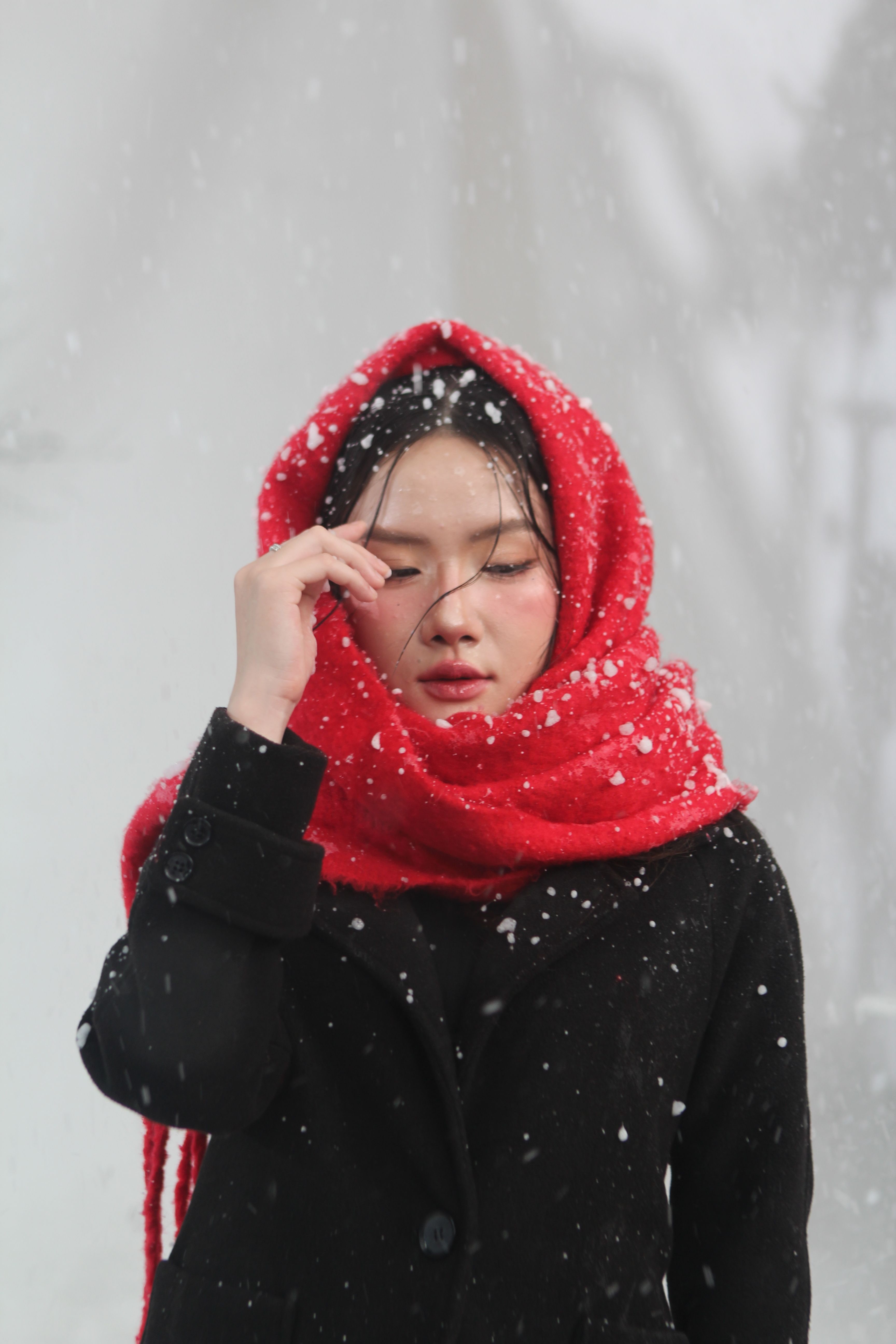 Portrait of a young woman in a red scarf during snowfall, conveying warmth and serenity.