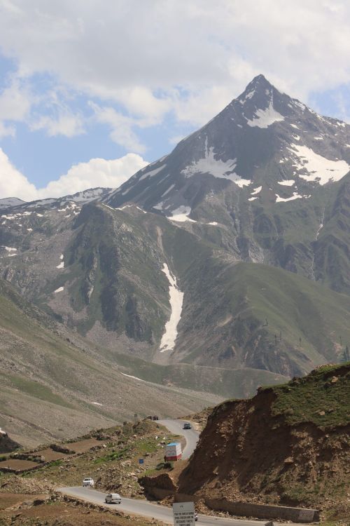 Free A winding road through a mountainous landscape with snow-capped peaks and clear sky. Stock Photo