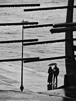 A couple shares an umbrella on a rainy day by the waterside in Istanbul, capturing urban serenity and romance.