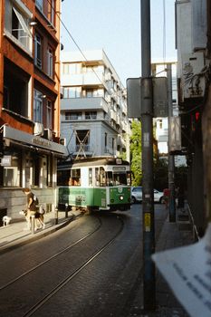 Historic tramway navigating a narrow street in Istanbul's Moda neighborhood during sunset.