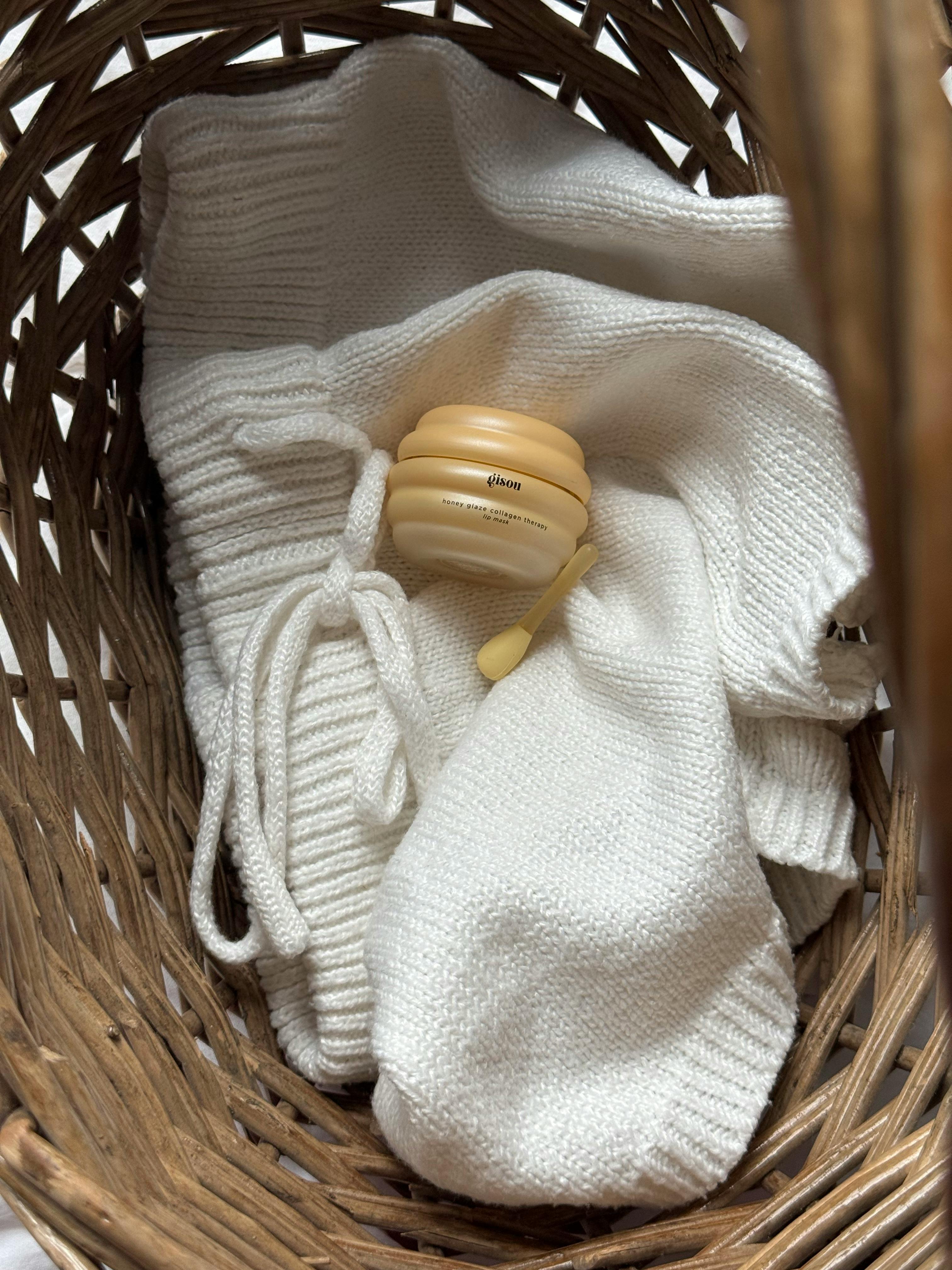 Soft white baby outfit in a wicker basket with baby cream jar.