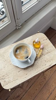 A cozy setup featuring a cup of coffee and essential oil bottles on a marble table by the window.