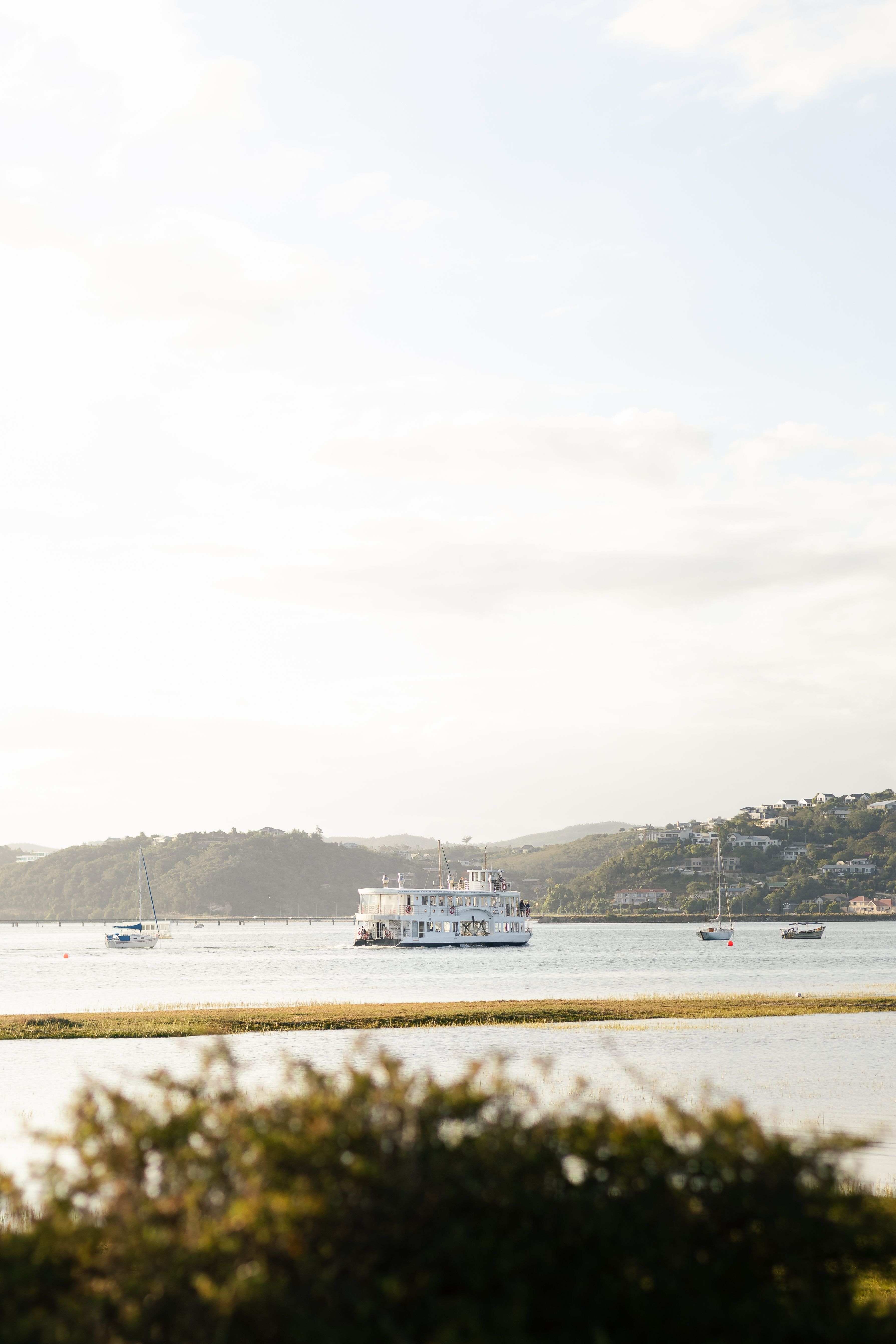 Peaceful river scene with a cruise boat and sailboats at sunset, perfect for travel and nature themes.