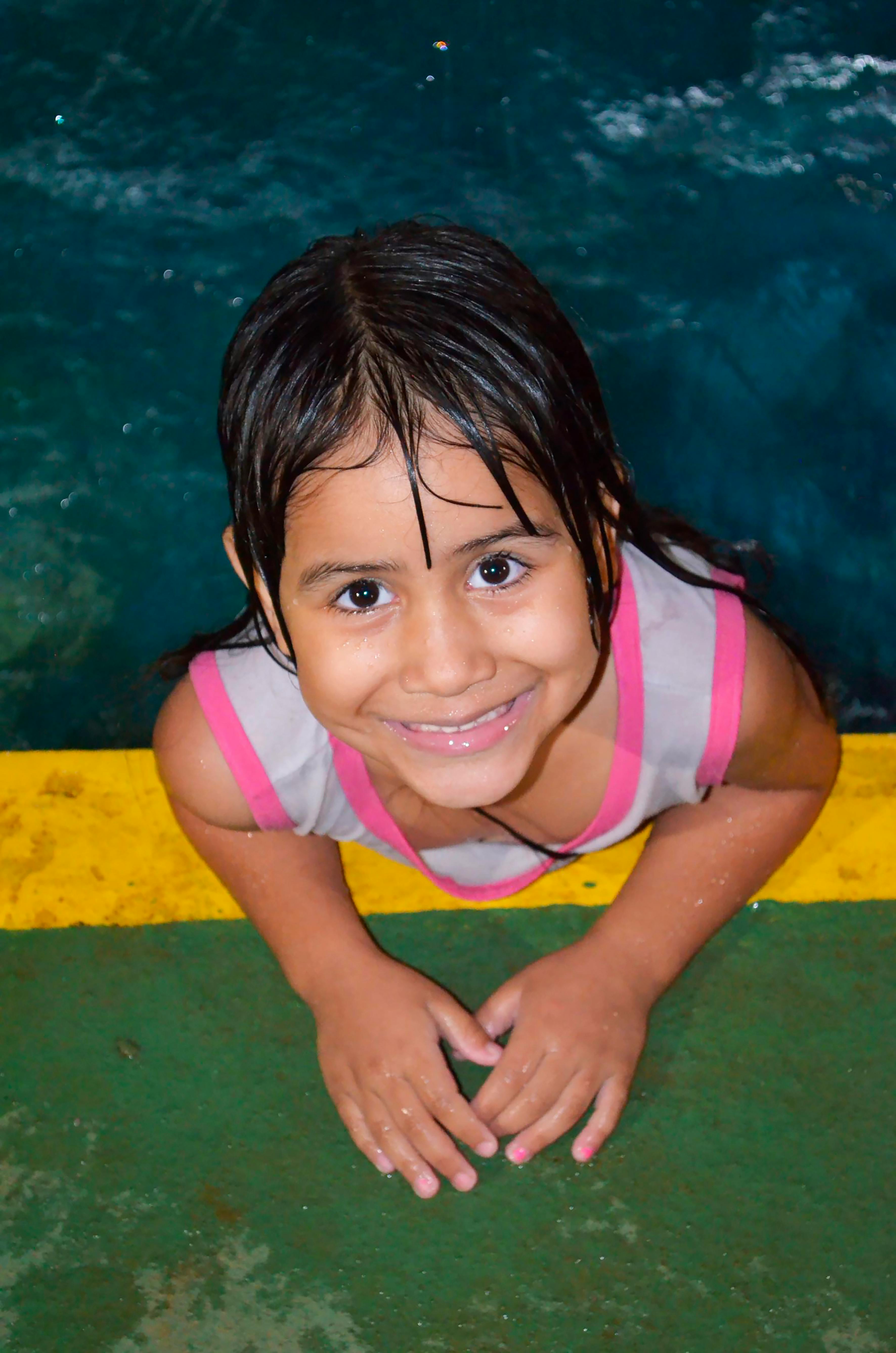 A joyful child enjoying a summer day at the pool, leaning against the edge with a bright smile.