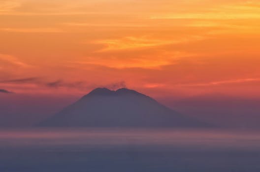 A mountain silhouette under a vibrant sunrise sky, creating a warm and tranquil scene.