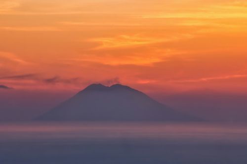 Free A mountain silhouette under a vibrant sunrise sky, creating a warm and tranquil scene. Stock Photo