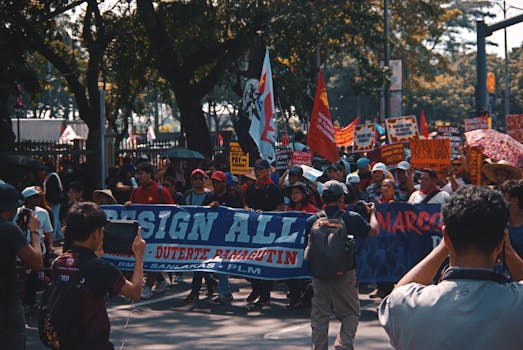 A large group of activists holding banners during a street protest under sunny skies.
