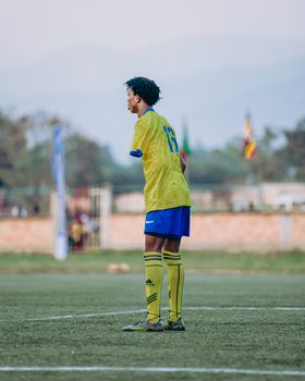 A young male soccer player in bright uniform stands focused on the field during a match.