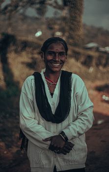 A smiling woman in traditional attire stands outdoors, exuding warmth and joy.