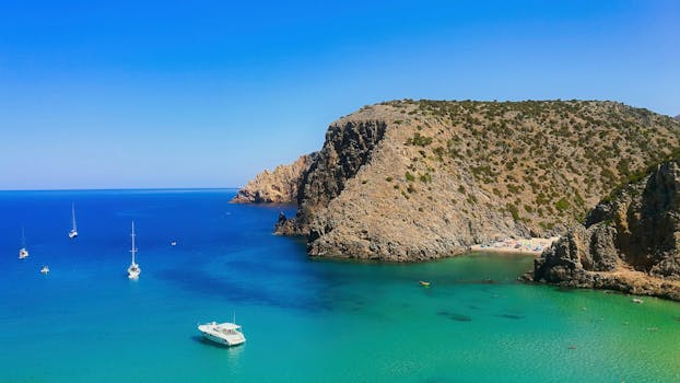 Scenic view of Cala Domestica Bay featuring boats and stunning rocky cliffs under a clear blue sky.
