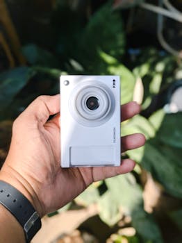 Close-up of a hand holding a digital camera with blurred green background.