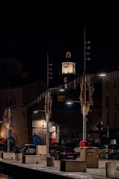 European town square illuminated at night with festive decorations and a clock tower.