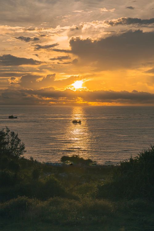 Free A breathtaking view of a golden sunset over a calm ocean with silhouetted boats. Stock Photo